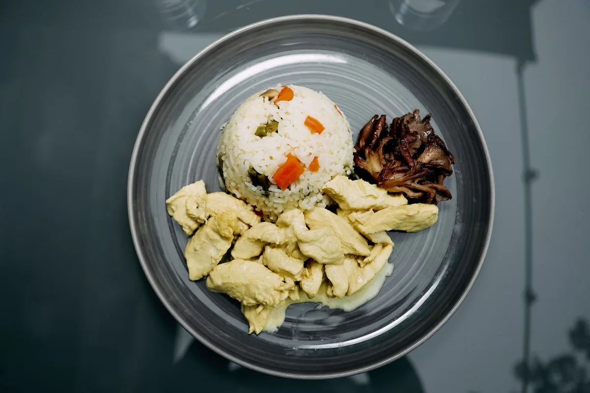 Bowl of boiled chicken and white rice on a kitchen counter, with a measuring cup beside it