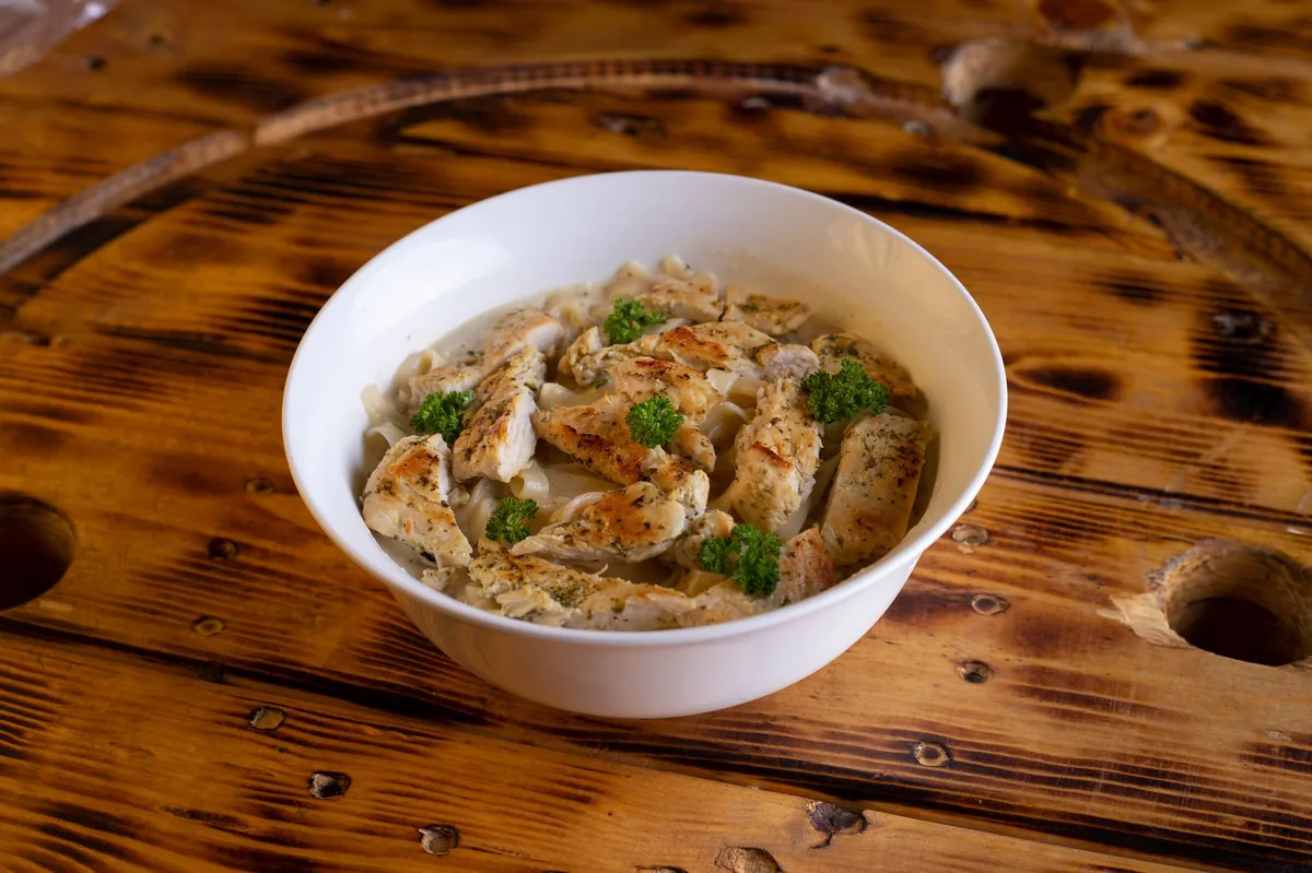 Freshly prepared home‑cooked dog meal in a bowl, featuring boiled chicken, rice, and carrots, with a fish oil capsule beside it